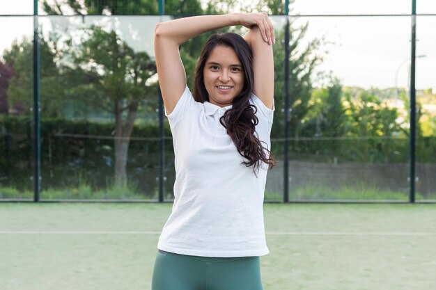 Sorridente giovane donna che si estende sul campo da paddle il giorno d'estate