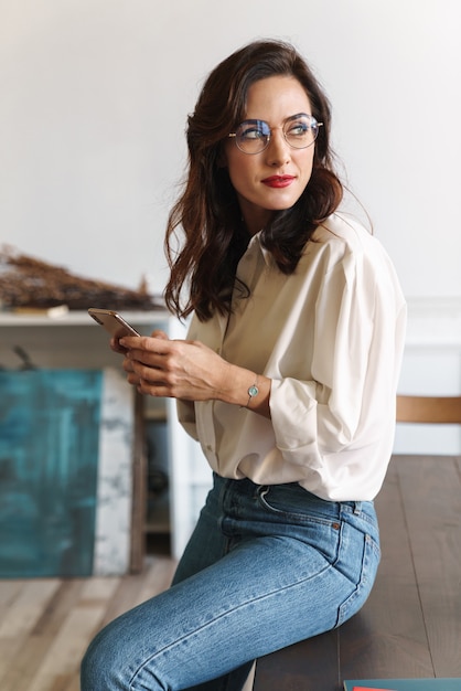 Sorridente giovane donna che utilizza il telefono cellulare mentre è seduto su un tavolo nella caffetteria al chiuso