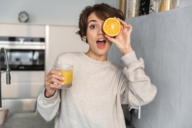 Sorridente giovane donna con succo d'arancia e frutta arancione mentre si trovava in cucina