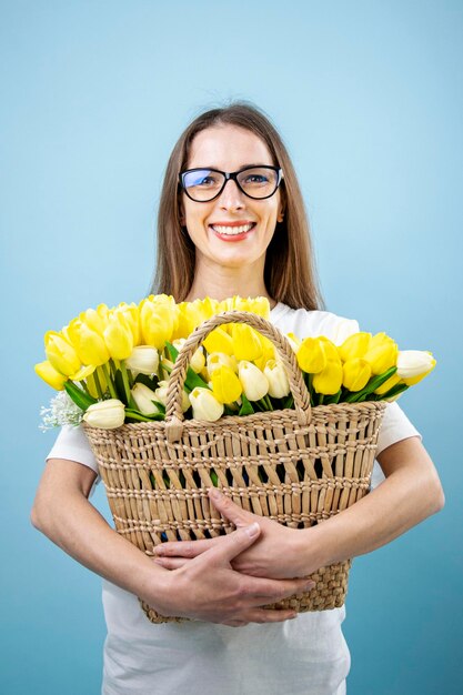 Sorridente giovane donna con tulipani gialli nel carrello su sfondo blu