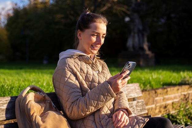 Sorridente giovane donna con un telefono seduto su una panchina nel parco