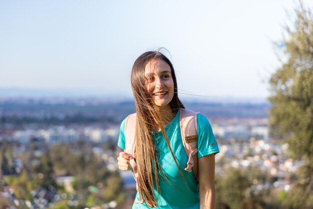 Sorridente giovane donna con uno zaino sulla cima di una collina. Fiducia in se stessi.