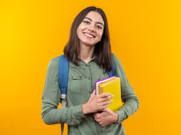 Sorridente giovane donna della scuola che indossa uno zaino in possesso di libri