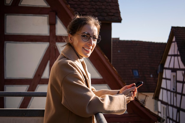 Sorridente giovane donna in cappotto con telefono in piedi sulla terrazza