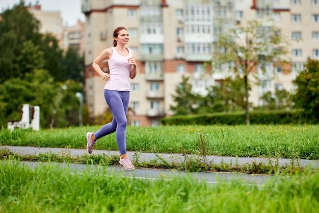 Sorridente giovane donna in leggins corre nel parco pubblico