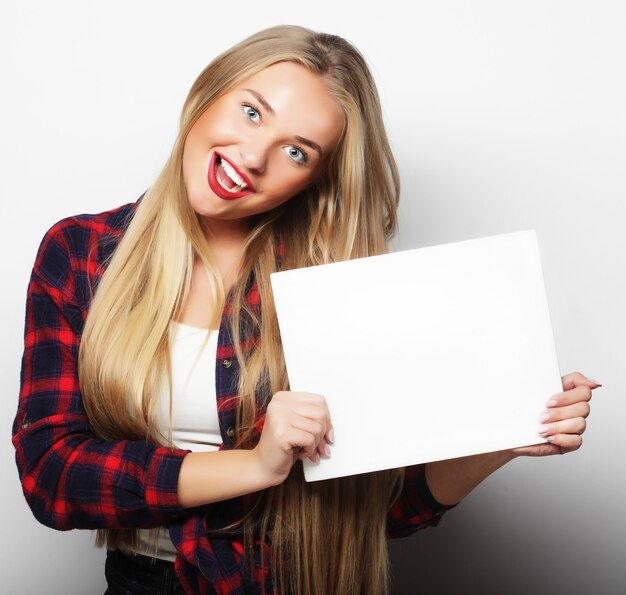 Sorridente giovane donna in stile casual che mostra cartello bianco, su sfondo bianco isolato