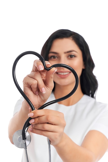 Sorridente giovane donna in uniforme medica che fa forma di cuore dallo stetoscopio