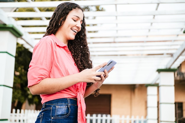 Sorridente giovane donna latinoamericana utilizzando un telefono cellulare