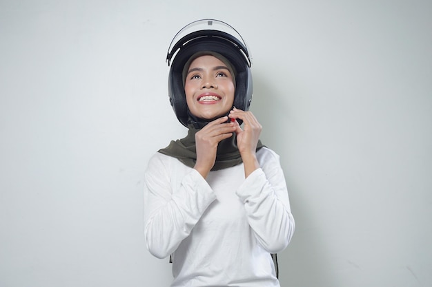 Sorridente giovane donna musulmana asiatica che utilizza il casco del motociclo isolato su priorità bassa bianca