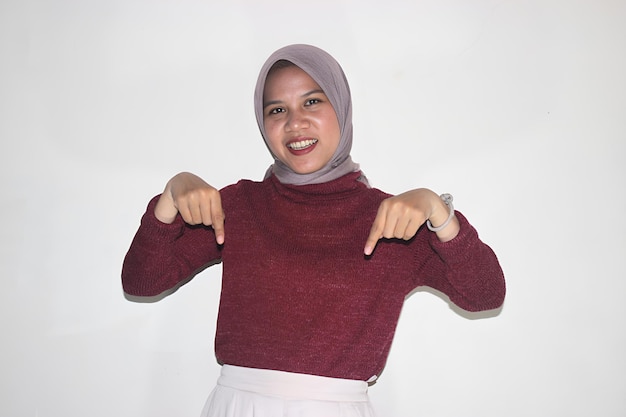 Sorridente giovane donna musulmana asiatica con hijab che punta le dita verso il basso