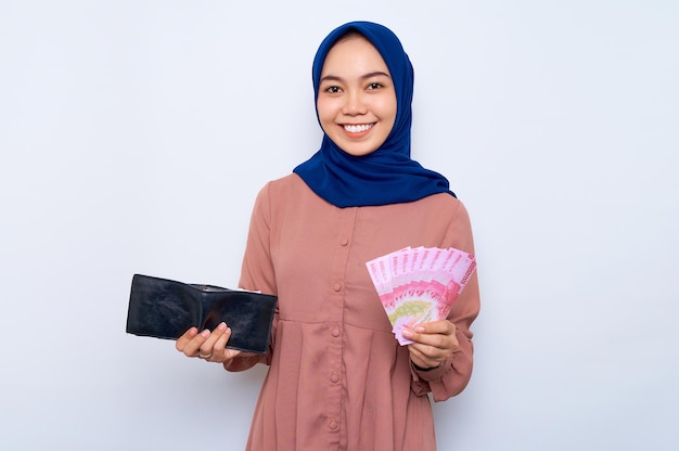 Sorridente giovane donna musulmana asiatica in camicia rosa azienda portafoglio e banconote denaro isolato su sfondo bianco Concetto di stile di vita della gente