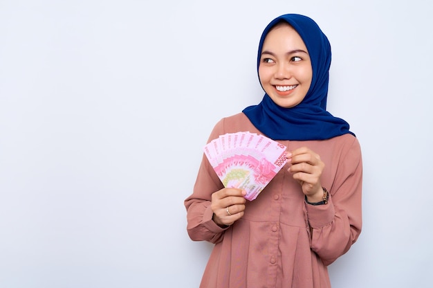 Sorridente giovane donna musulmana asiatica in camicia rosa in possesso di banconote denaro isolato su sfondo bianco Concetto di stile di vita religioso della gente