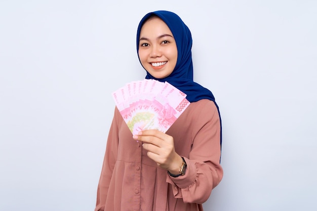 Sorridente giovane donna musulmana asiatica in camicia rosa in possesso di banconote denaro isolato su sfondo bianco Concetto di stile di vita religioso della gente