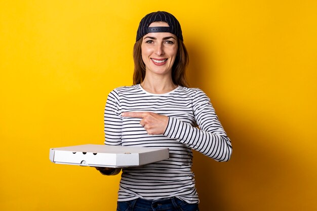 Sorridente giovane donna pizza consegna uomo, punta il dito sul lato tenendo la pizza su giallo