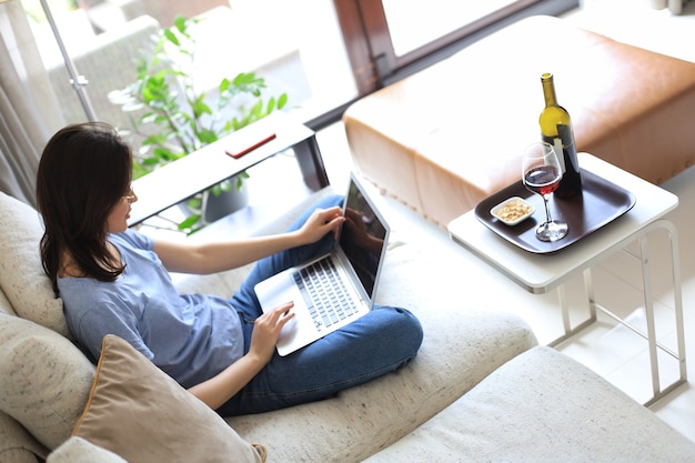 Sorridente giovane donna seduta sul divano con il computer portatile e chattare con gli amici. Vista dall'alto.