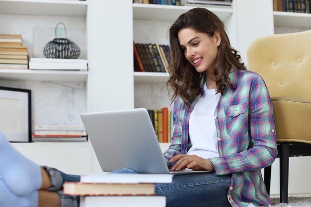 Sorridente giovane donna seduta sul pavimento in soggiorno studentessa che studia a casa lavorando con il suo computer portatile. Insegnamento a distanza