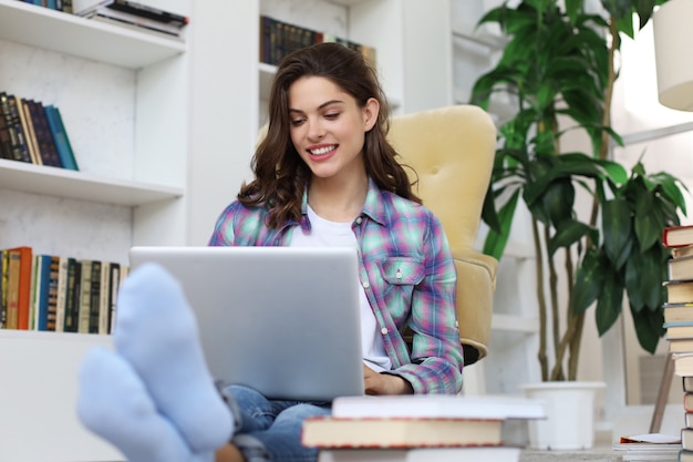 Sorridente giovane donna seduta sul pavimento in soggiorno studentessa che studia a casa lavorando con il suo computer portatile.