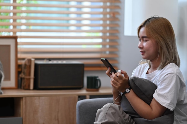 Sorridente giovane donna ubicazione sul divano e utilizzando smart phone