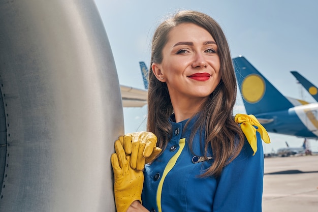 Sorridente giovane hostess in guanti di pelle appoggiata sulla fusoliera dell'aereo