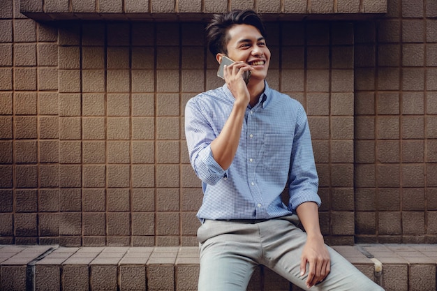 Sorridente giovane imprenditore asiatico utilizzando il telefono cellulare in città