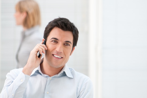 Sorridente giovane imprenditore parlando al cellulare al lavoro in ufficio