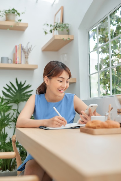 Sorridente giovane imprenditrice asiatica seduta a un tavolo e scrivere note