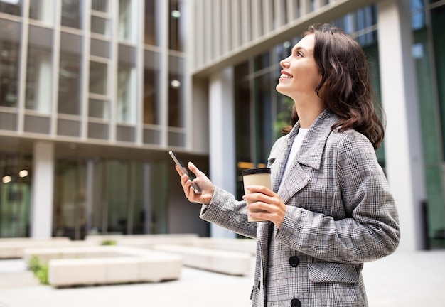 Sorridente giovane imprenditrice utilizzando il cellulare nell'area urbana della città