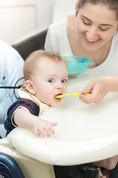 Sorridente giovane madre che allatta il suo bambino nel seggiolone