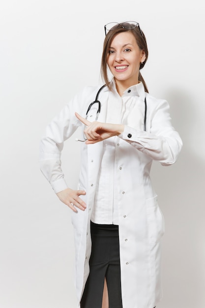 Sorridente giovane medico donna con stetoscopio, occhiali isolati su sfondo bianco. Medico femminile in abito medico che indica dito indice da parte sullo spazio della copia. Concetto di medicina della salute del personale sanitario