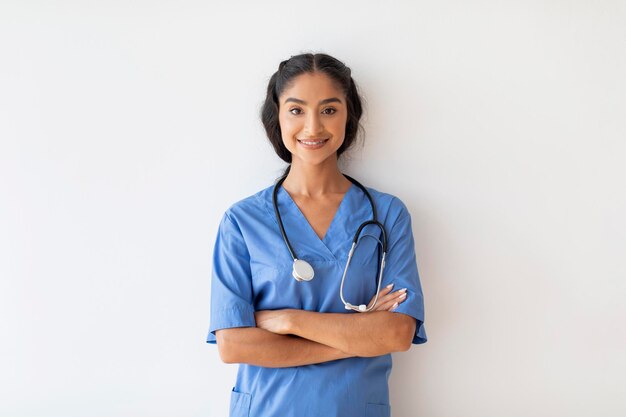 Sorridente giovane medico indiano donna in uniforme in posa su sfondo bianco