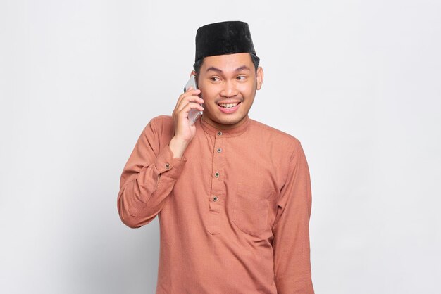 Sorridente giovane musulmano asiatico parlando al telefono cellulare isolato su sfondo bianco