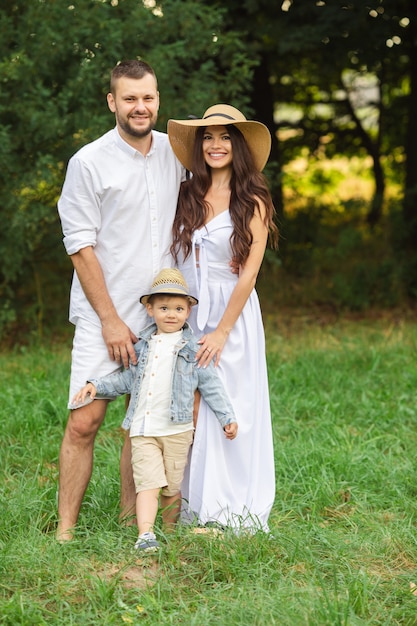 Sorridente giovane padre e madre in piedi con il loro piccolo figlio mentre si gode il fine settimana del giorno d'estate. Famiglia e concetto di svago