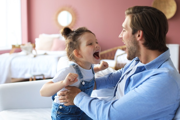 Sorridente giovane padre sdraiato sul divano in soggiorno e gioca con la piccola figlia felice.