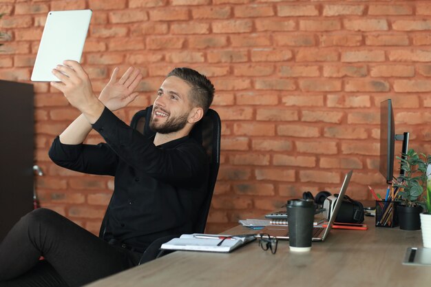 Sorridente giovane prendendo selfie da smartphone o avendo videochiamata in ufficio.