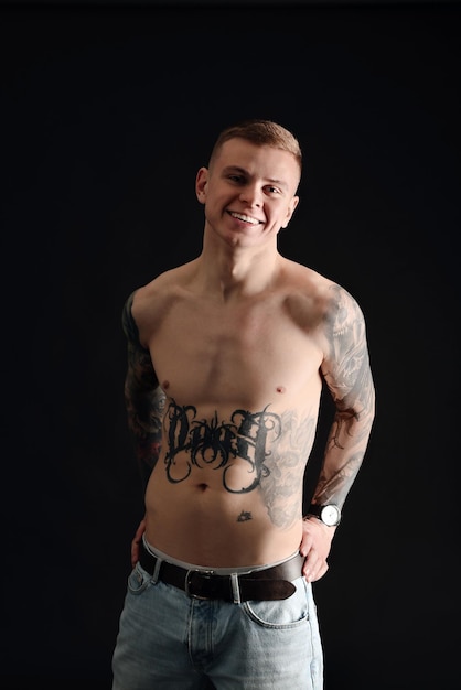 Sorridente giovane senza camicia con tatuaggi su sfondo nero