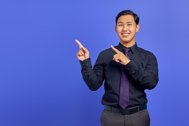 Sorridente giovane uomo asiatico che punta il dito sullo spazio della copia su sfondo viola