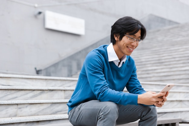 Sorridente giovane uomo asiatico parlando al telefono cellulare mentre era seduto sulle scale all'aperto