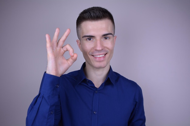 Sorridente giovane uomo bello in camicia blu fa il segno OK