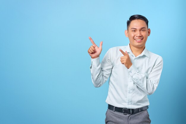 Sorridente giovane uomo d'affari bello che punta il dito sullo spazio della copia su sfondo blu