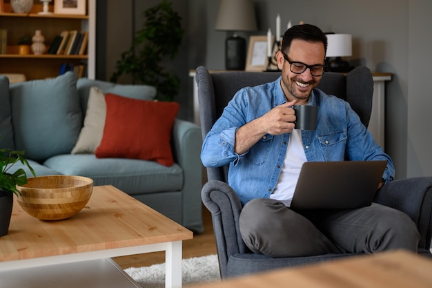 Sorridente giovane uomo d'affari che beve caffè e legge i messaggi di posta elettronica sul computer wireless