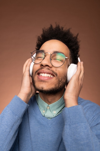 Sorridente giovane uomo d'affari di razza mista che tiene gli occhi chiusi mentre si gode musica piacevole in cuffia davanti alla telecamera