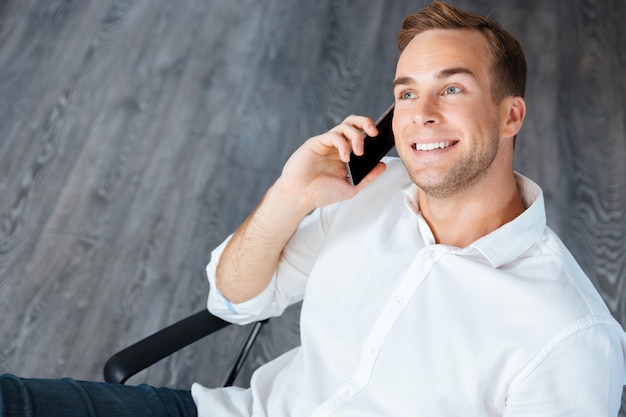 Sorridente giovane uomo d'affari seduto e parlando al telefono cellulare in ufficio