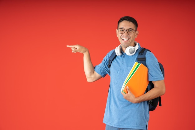 Sorridente giovane uomo del college con gli occhiali che tiene i suoi quaderni puntando il dito indice