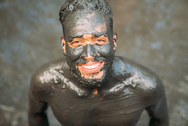 Sorridente giovane uomo latino-americano che fa il trattamento con argilla verde