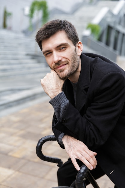 Sorridente giovane uomo vestito di cappotto appoggiato su una bicicletta su una strada