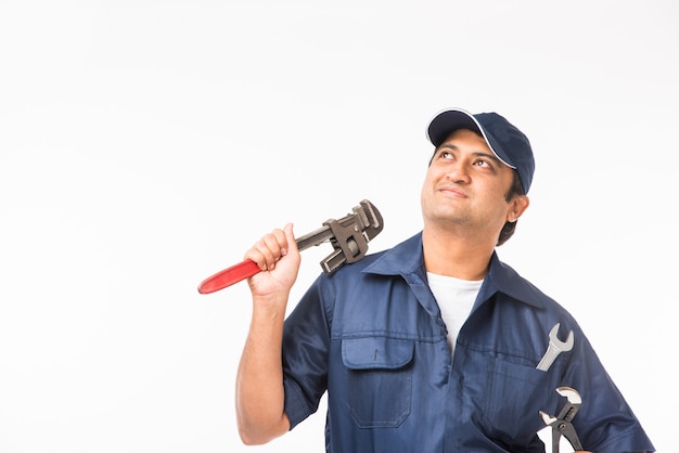 Sorridente idraulico indiano con chiave a tubo o chiave idraulica, indossando l'uniforme blu con cappuccio che mostra i pollici in su. isolato