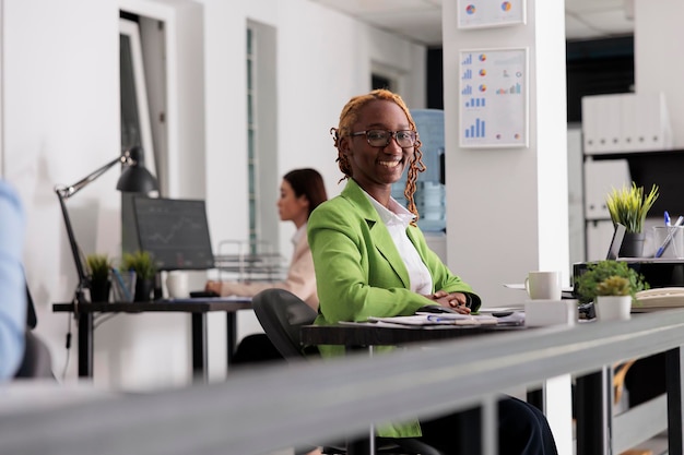 Sorridente impiegato di successo che lavora nello spazio di coworking, seduto alla scrivania, guardando la fotocamera. Donna attraente allegra con il ritratto di occhiali sul posto di lavoro dell'ufficio affari di unicorno