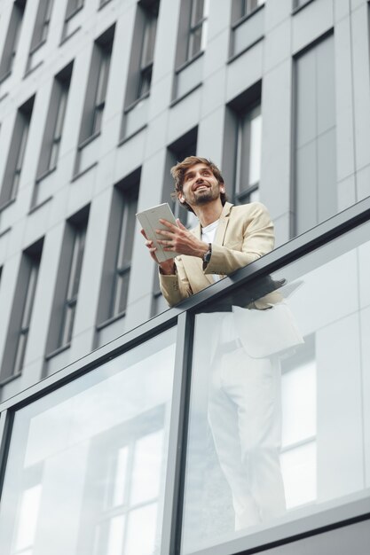 Sorridente imprenditore fiducioso in abito formale utilizzando tavoletta digitale per il lavoro. Inquadratura dal basso