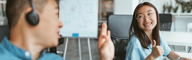 Sorridente imprenditrice asiatica che lavora al computer seduto in coworking sullo sfondo dei colleghi