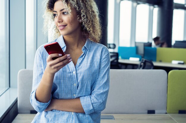 Sorridente imprenditrice utilizzando smartphone in ufficio. Indossare in camicia blu.